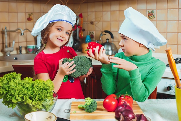 Crianças felizes e engraçadas da família estão preparando uma salada de legumes fresca na cozinha