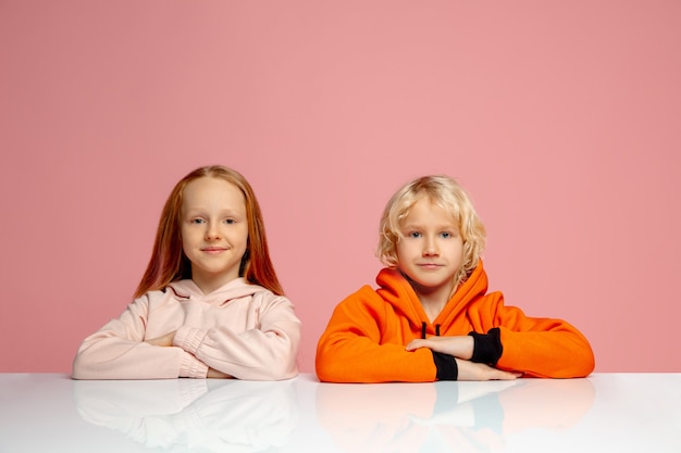 Crianças felizes isoladas no fundo do estúdio rosa coral. Parece feliz, alegre, sincero. Copyspace. Infância, educação, conceito de emoções