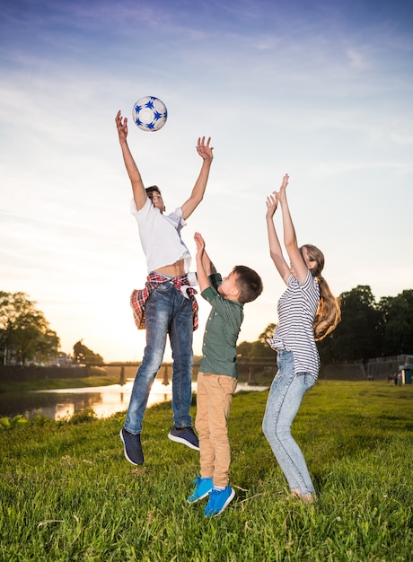 Crianças felizes pulando e brincando com bola ao ar livre. dia ensolarado de verão Foto Premium