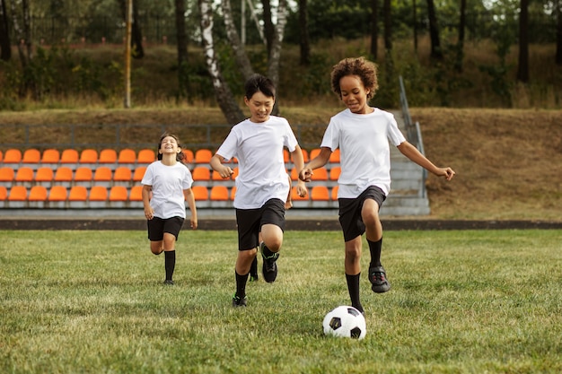 Crianças jogando futebol supervisionadas por treinador de futebol