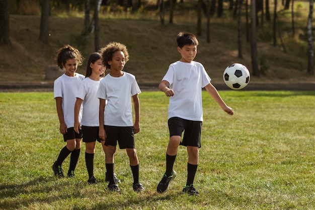 Foto grátis crianças jogando futebol supervisionadas por treinador de futebol