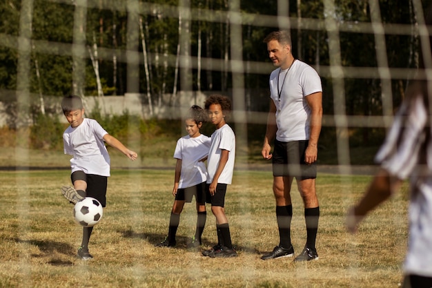 Foto grátis crianças jogando futebol supervisionadas por treinador de futebol