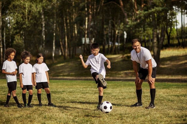 Crianças jogando futebol supervisionadas por treinador de futebol