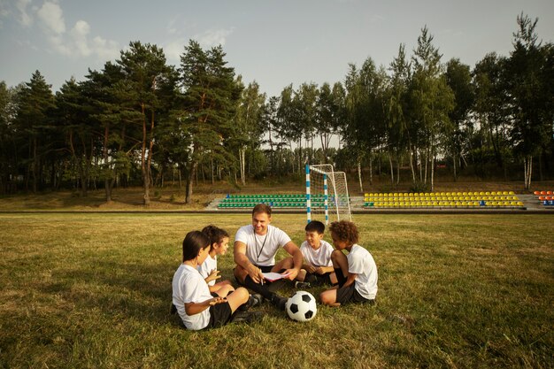 Crianças jogando futebol supervisionadas por treinador de futebol