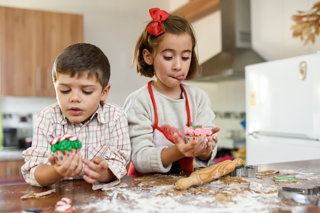 Crianças que comem bolinhos do Natal e bolinhos na cozinha