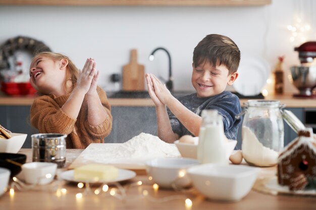 Crianças se agarrando com farinha enquanto assam biscoitos de Natal