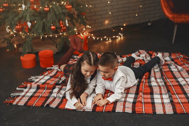 Crianças sentadas perto da árvore de Natal. As crianças escrevem uma carta ao Pai Natal.