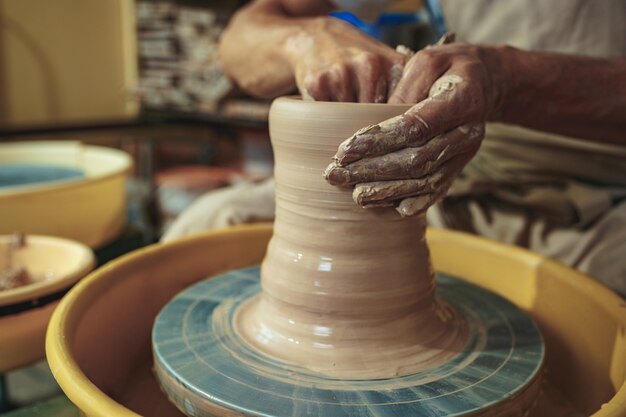 Criando uma jarra ou vaso de close-up de argila branca. Mestre crock. Mãos de homem fazendo macro de jarro de barro. O escultor na oficina faz uma jarra com um close de cerâmica. Roda de oleiro torcida.