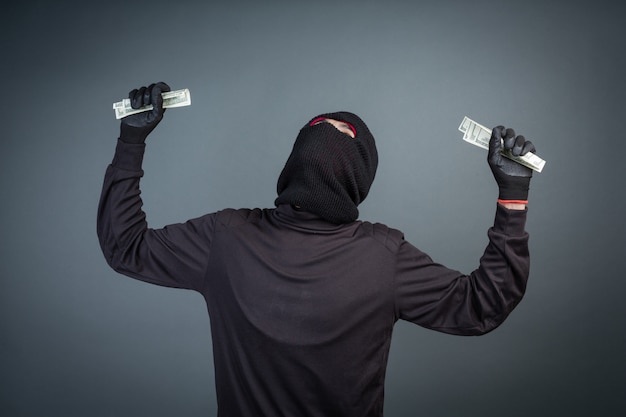 Foto grátis criminosos usam máscaras negras para segurar cartões de dólar em cinza