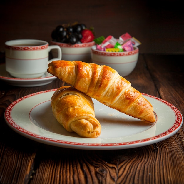 Croissant caseiro de close-up com uma xícara de chá, doces e frutas na mesa de madeira