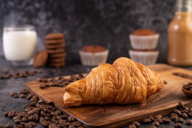 Croissant colocado em uma plataforma de madeira com grãos de café em um piso de cimento preto.