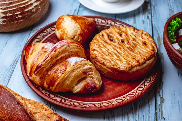 Croissant de assados de vista lateral com açúcar em pó e massa folhada em um prato