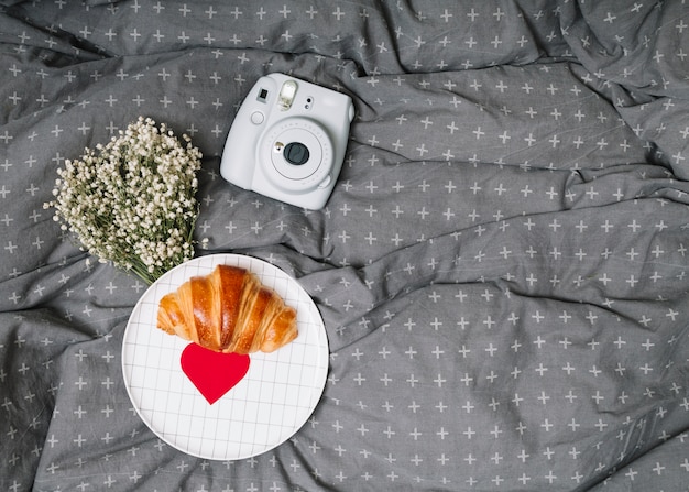 Foto grátis croissant e enfeite de papel coração no prato perto de plantas e câmera