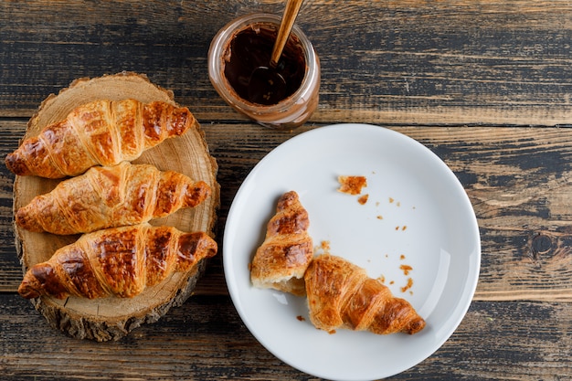 Croissant em um prato com creme de chocolate plano leigos na tábua de madeira e