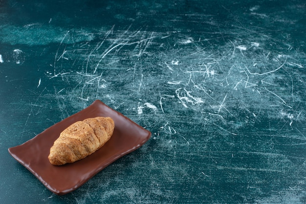Croissant em um prato marrom, sobre o fundo azul. Foto de alta qualidade