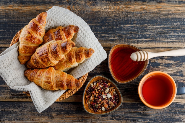 Croissant em uma cesta com mel, concha, chá, ervas secas planas deitado em uma mesa de madeira