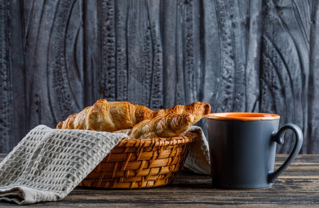 Croissant em uma cesta com xícara de chá vista lateral em uma mesa de madeira