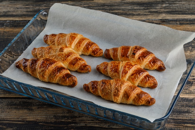 Foto grátis croissant em uma placa de vidro alto ângulo vista sobre uma mesa de madeira