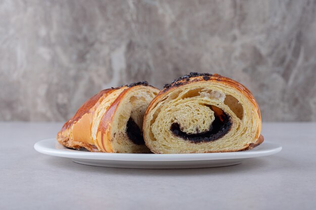 Croissant fatiado caseiro com chocolate em um prato na mesa de mármore.