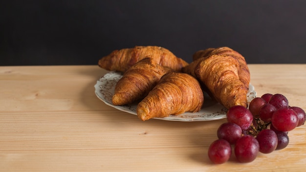 Croissants cozidos na placa cerâmica e uvas maduras na mesa de madeira