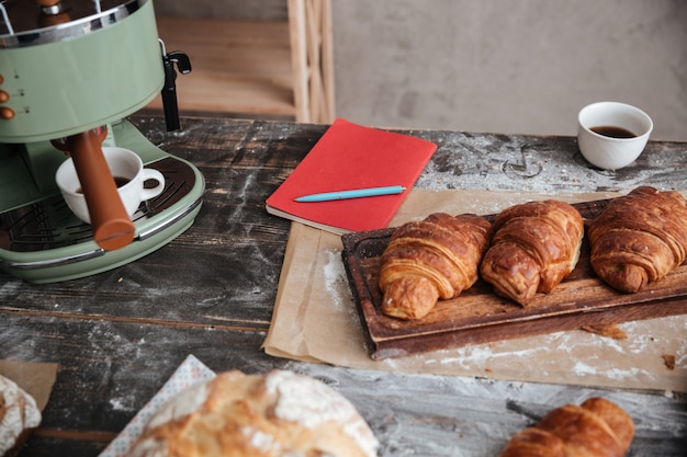 Croissants de pastelaria na mesa perto de xícara de café e notebook.