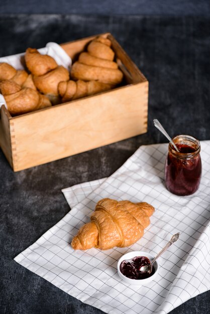 croissants em caixa de madeira e panela com geléia de lado na mesa cinza