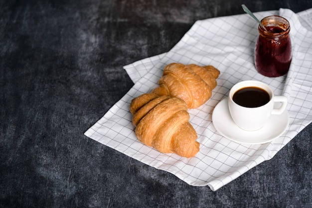 croissants, panela com geléia e xícara de café à parte na mesa cinza