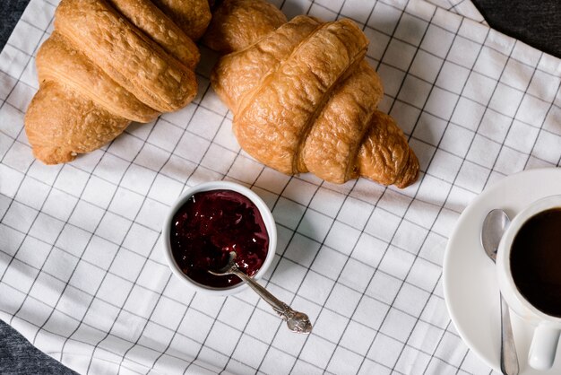 croissants, panela com geléia e xícara de café à parte na mesa cinza