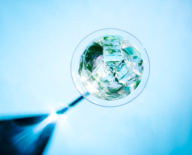 Cubos de gelo de cristal no copo de martini com sombra brilhante no fundo azul
