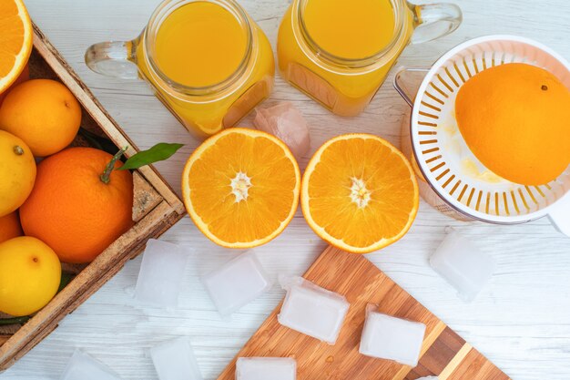 cubos de gelo de vista superior na tábua de madeira na frente de copos de suco de laranja