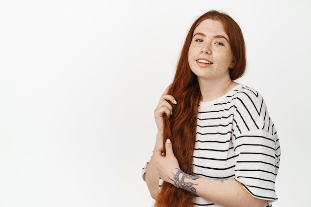 Cuidado e estilo do cabelo. Mulher linda ruiva escovando seu longo cabelo ruivo ruivo usando uma camiseta casual branca