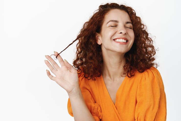 Foto grátis cuidados com a pele da beleza. retrato de uma jovem natural com cabelo ruivo encaracolado, rindo feliz, dentes de sorriso branco, brincando com o cabelo, em pé despreocupado contra o fundo branco