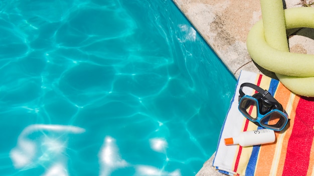 Óculos de proteção com loção na toalha perto de brinquedo e piscina