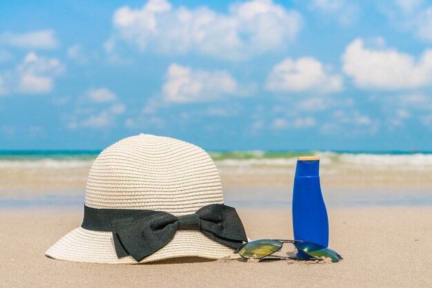 Óculos de sol, protetor solar e chapéu na praia de areia branca