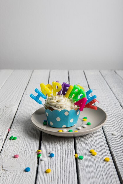 Cupcake com velas coloridas de aniversário e doces na mesa de madeira texturizada