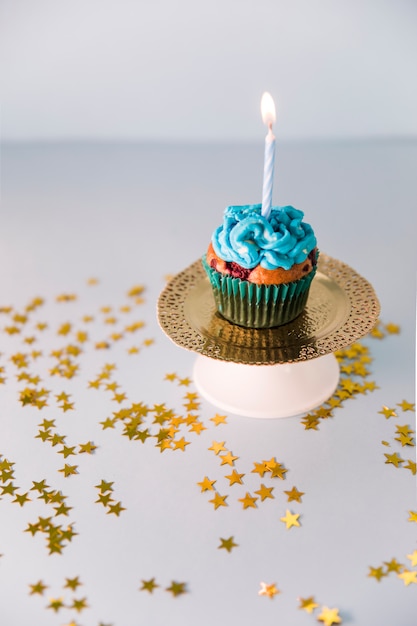 Cupcake de aniversário delicioso com vela acesa na placa dourada