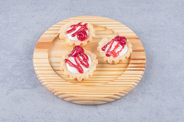 Cupcakes com cobertura de calda de morango em travessa de madeira sobre mármore