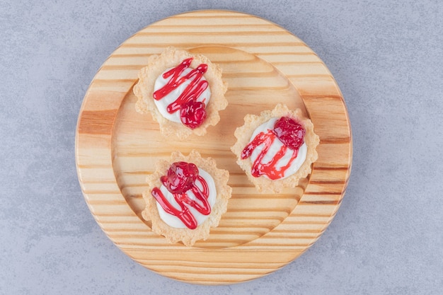 Cupcakes com cobertura de calda de morango em uma travessa de madeira na mesa de mármore.