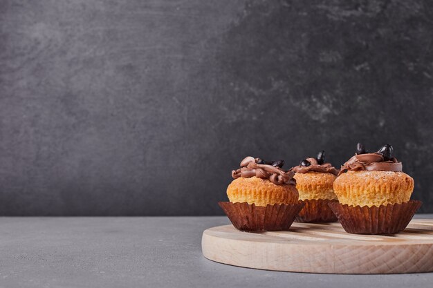 Cupcakes com creme de chocolate na travessa de madeira.