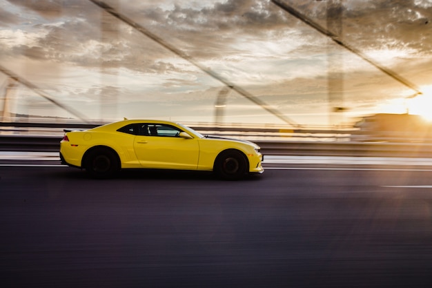 Cupê amarelo do esporte na estrada no por do sol.