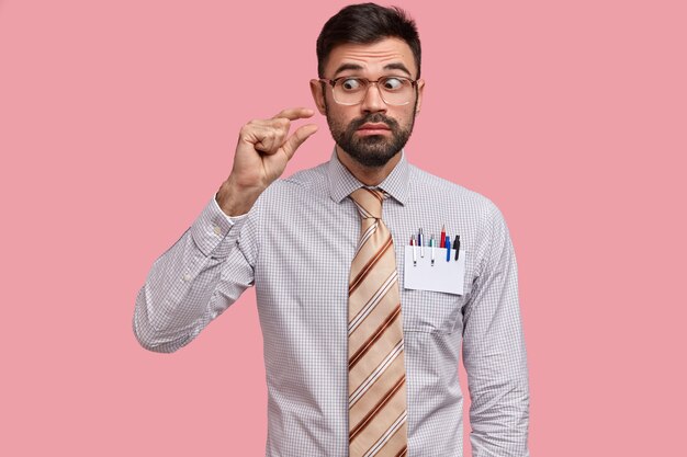 Curioso, jovem diretor com a barba por fazer mostra um pequeno objeto, vestido com roupa formal, gesticulando com a mão