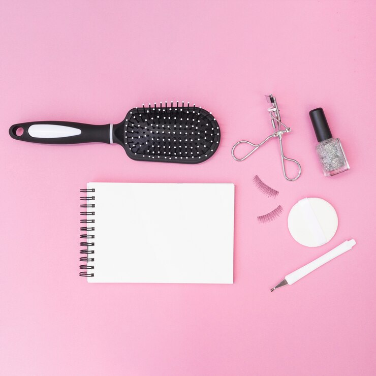 Foto grátis cutícula; escova de cabelo; esponja; pestanas falsas; curvex de cílios; garrafa de esmalte com bloco de notas em branco espiral no pano de fundo rosa
