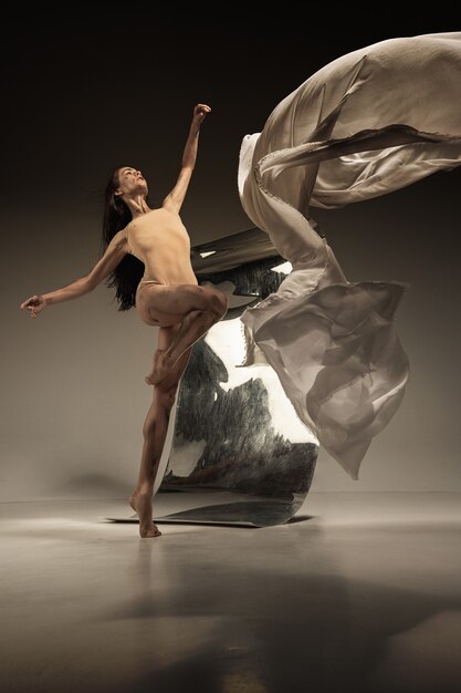 Dançarina de balé jovem e elegante na parede marrom com espelho