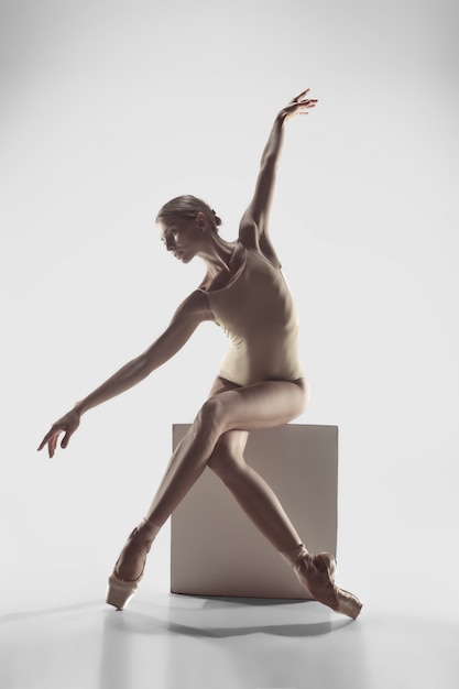 Dançarino de bailado feminino gracioso jovem ou bailarina clássica dançando no estúdio branco.