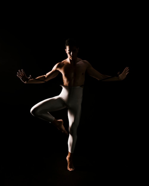 Dançarino do sexo masculino em pé contra um fundo preto com as mãos estendidas