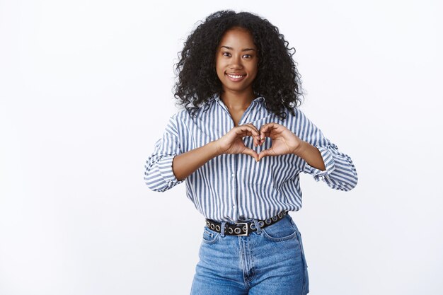 De aparência amigável, encantadora jovem morena feliz mostrando coração gesto romântico sinal de amor sorrindo amplamente sentindo simpatia confessando namorado sentimentos reconfortantes, conceito de relacionamento