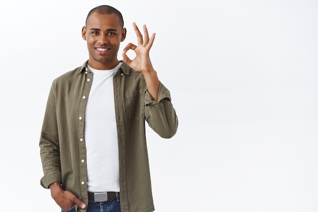 De boa qualidade, garanto que gostou. Retrato de homem afro-americano confiante mostrando tudo bem, sinal de ok e sorrindo, aceno com a cabeça em aprovação