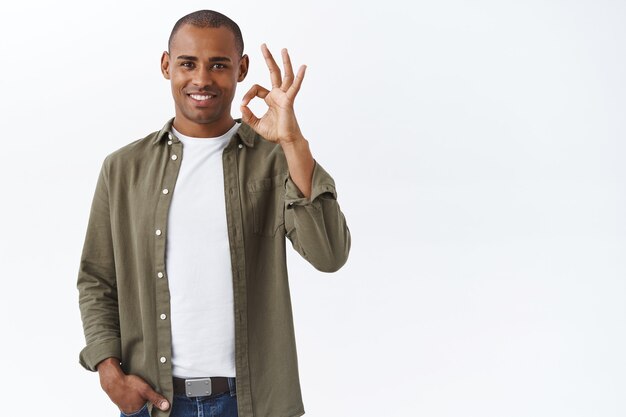 De boa qualidade, garanto que gostou. Retrato de homem afro-americano confiante mostrando tudo bem, sinal de ok e sorrindo, aceno com a cabeça em aprovação