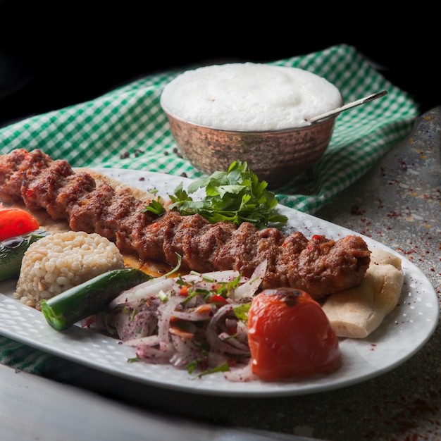 De cima adana kebab com arroz e legumes fritos e cebola picada e ayran