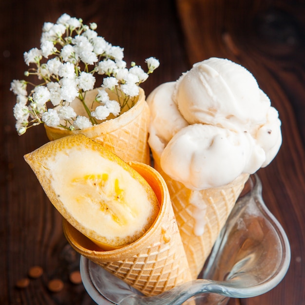 De cima, cones de waffle com sorvete de banana e fatias de banana e gypsophila em uma xícara de sorvete